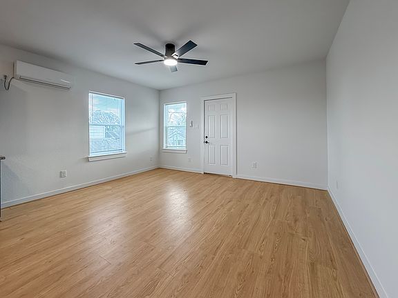 Bright, spacious room with light wood flooring, white walls, and a ceiling fan. Features a mini-split AC unit and two windows for natural light. Ideal for a bedroom or office space.