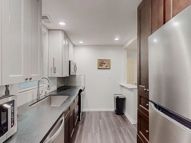 Efficient galley kitchen with stainless appliances, generous cabinetry, and long counters plus a pass-through to the next roo