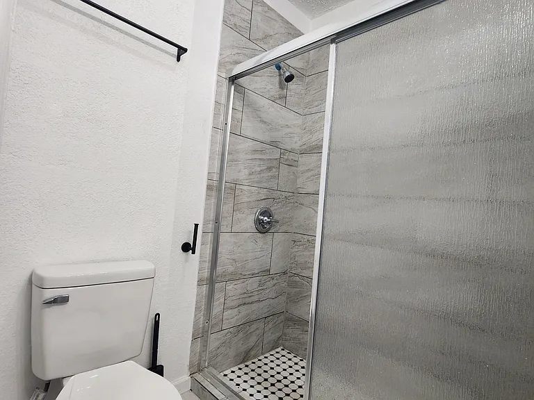 Updated bathroom featuring a tiled walk-in shower with sliding glass doors and easy-care tile flooring.