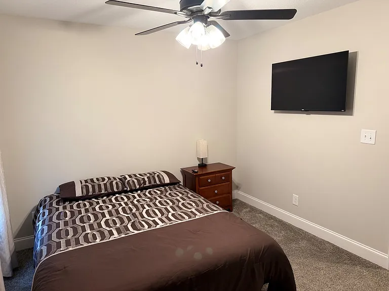 Furnished bedroom with a ceiling fan, wall-mounted TV, and nightstand for convenient everyday storage.