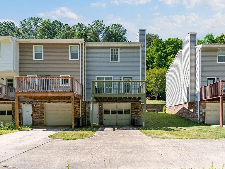 Rear exterior view showcasing the attached garage, private driveway, and elevated back deck overlooking the grassy common area