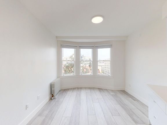 Bright, empty room with wood-like flooring, a bay window, featuring minimalist cabinetry, natural light abundant