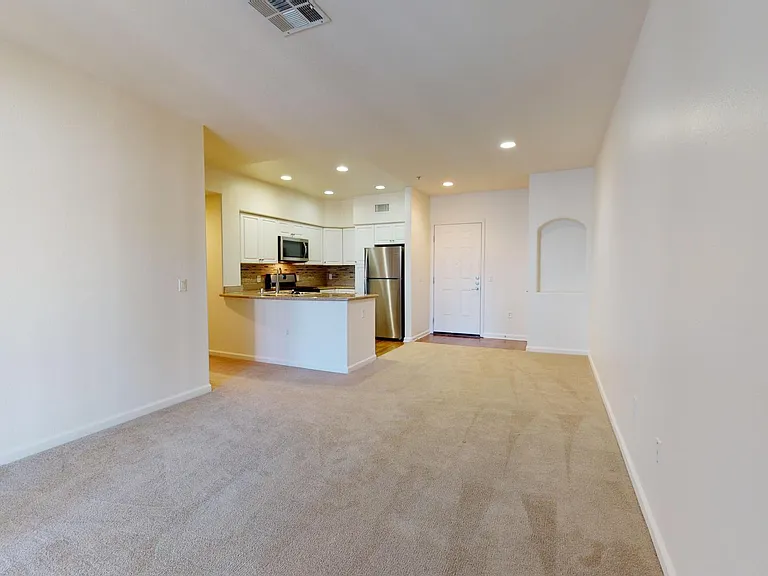 Apartment kitchen with stainless steel appliances, dining and living room with plush carpet flooring.