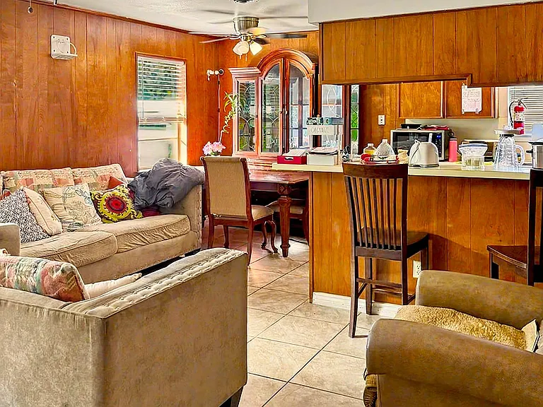 Open living area with tile flooring, ceiling fans, and an adjacent breakfast bar that connects to the kitchen.