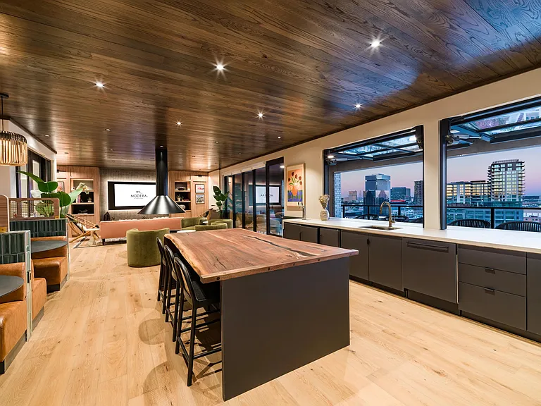 An inviting clubroom kitchen in our sky lounge with a warm wood island, open seating, and expansive windows framing downtown Dallas views.