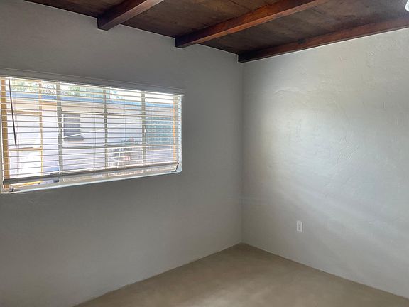 Bedroom with wood beam ceilings. Floors are grey concrete overlay.