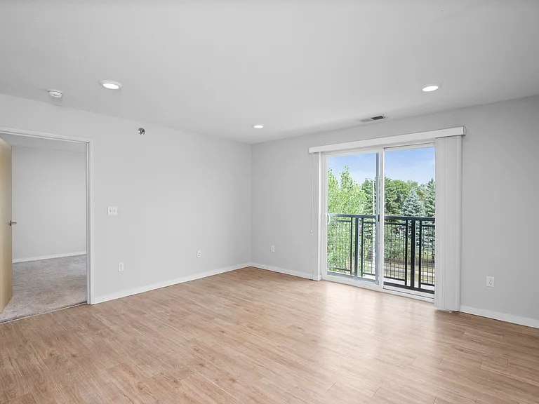 Bright and airy living room with sleek hardwood floors, a sliding glass door leading to a balcony with lush green views, and modern recessed lighting. Bright and airy living room with sleek hardwood floors, a sliding glass door leading to a balcony with l