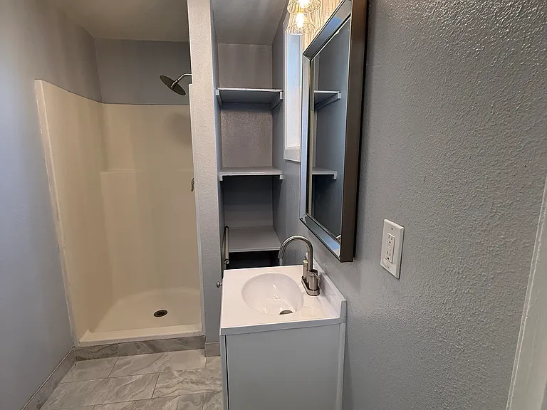 Bathroom with shower. New sink, new sink cabinet, new mirror, new window, new lighting fixtures, new bath fan, new tile flooring, new toilet, fresh paint, new shower hardware.