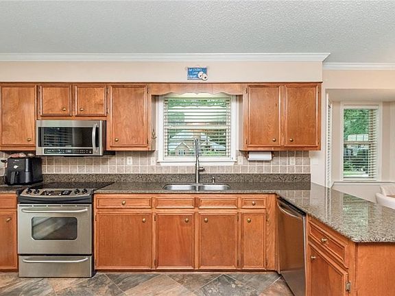 Kitchen featuring wood cabinetry, stainless steel appliances, speckled countertops, a tile backsplash, and bay windows