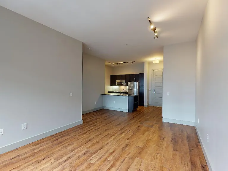 Apartment kitchen with stainless steel appliances, dining and living room with wood-style flooring.