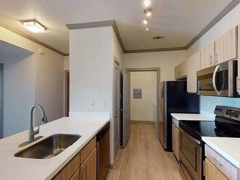 Apartment kitchen with stainless steel appliances, quartz countertops and wood-style flooring.