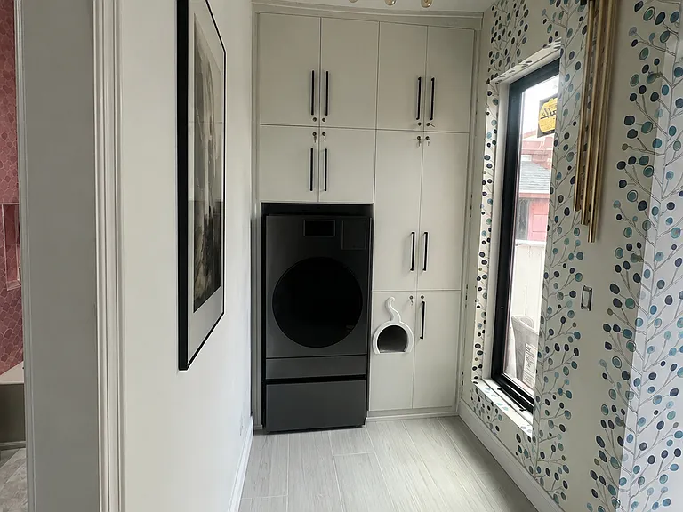 Dedicated laundry area with a sleek, energy-efficient washer/dryer, extensive custom floor-to-ceiling cabinetry, and a charming built-in cat hideaway.