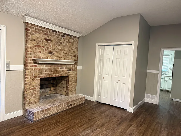 Living area with a brick fireplace and mantle, durable wood-look flooring, and adjacent closet for extra storage.