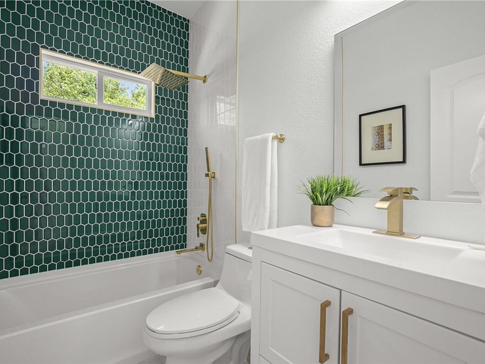 High end gold finishes elevate the captivating emerald green tiling in this spacious shared bathroom. Peak that rainshower!