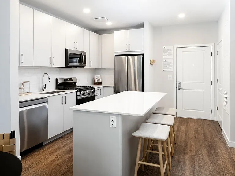 Showroom kitchen with stainless steel appliances, white quartz countertop, light grey cabinetry, and hard surface flooring