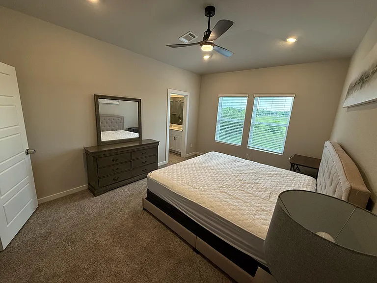 Spacious bedroom with ceiling fan, large windows, and convenient access to an en-suite bath plus dresser storage.