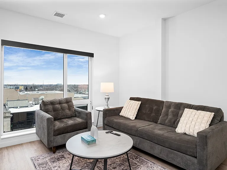 Chic and cozy living room with modern furniture, large window offering scenic city views, and stylish decor. Chic and cozy living room with modern furniture, large window offering scenic city views, and stylish decor.