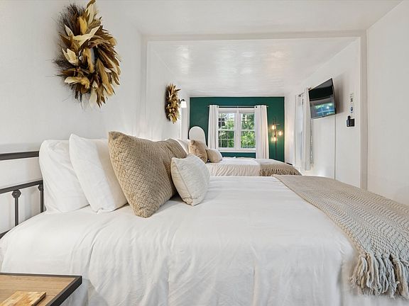 Feather wreaths crown each queen bed, adding soft style. Cozy blankets, plush pillows, and bedside touches create a warm South Bend guest retreat near Notre Dame_perfect for restful nights. One of the beds can be removed as desired.