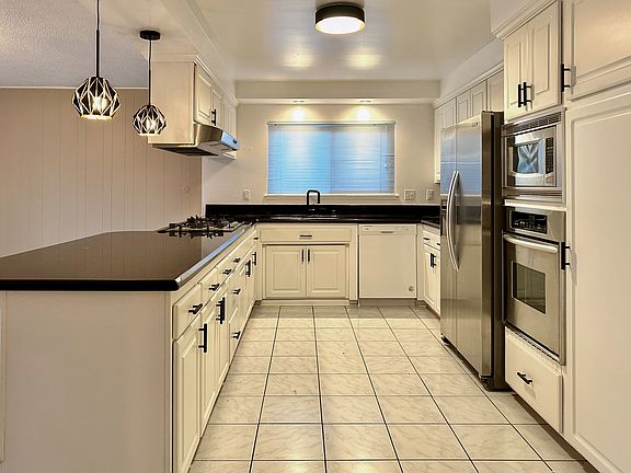 Large kitchen with gas cooktop, stainless steel appliances (fridge with water filter and ice maker), microwave, oven, dishwasher, large peninsula with overhang counter seating, opens to dining room and slider door leading to backyard.