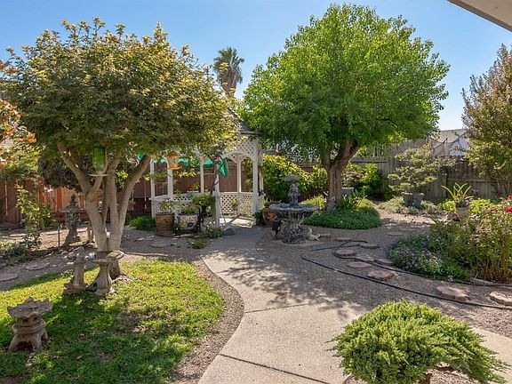 Fully landscaped backyard with gazebo, birdbath, mature trees, and statuary.