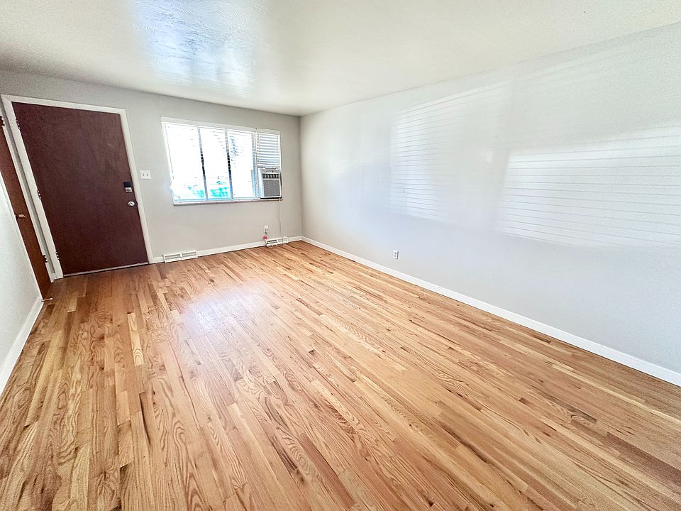 Bright and inviting living room with elegant hardwood floors, a large window, and sleek white walls.