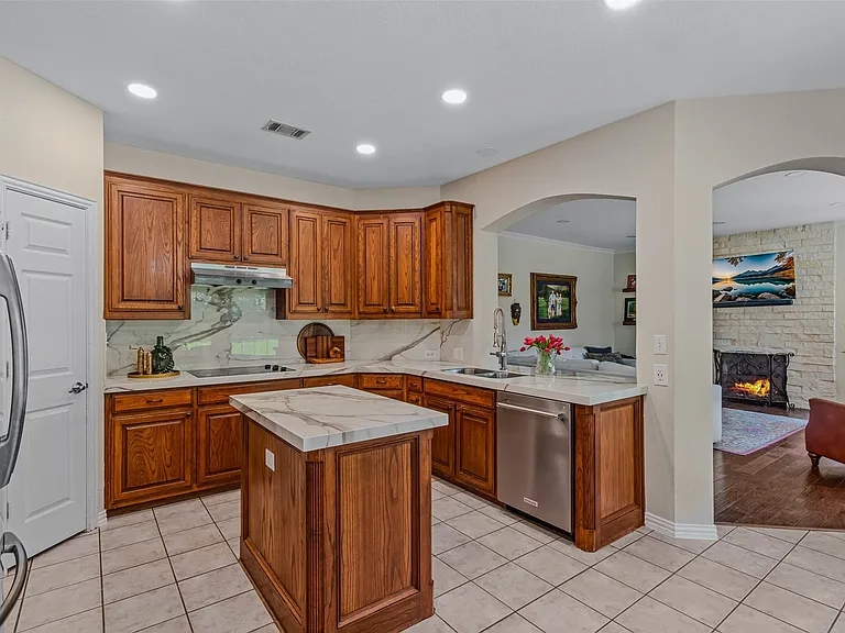 Kitchen featuring wood cabinetry, stone countertops with a matching backsplash, stainless steel appliances, and a central island