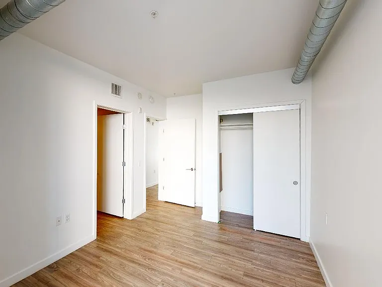 Spacious apartment bedroom with attached bathroom and wood-style flooring.