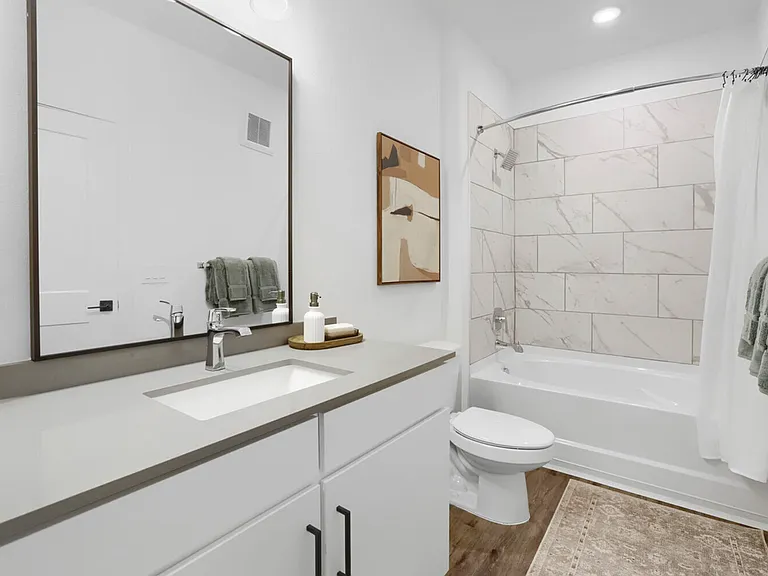 Spa-inspired finishes, every morning. The B2 primary bathroom showcases a quartz vanity, large black-framed mirror, and a marble-look tiled tub surround that elevates the everyday routine.