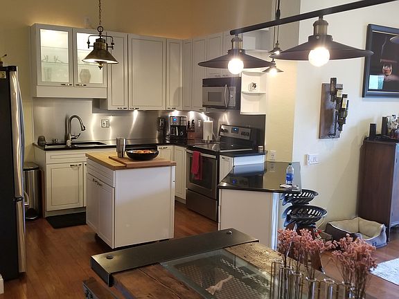 Dining room table in foreground, kitchen in background with stove, microwave and bar seating.