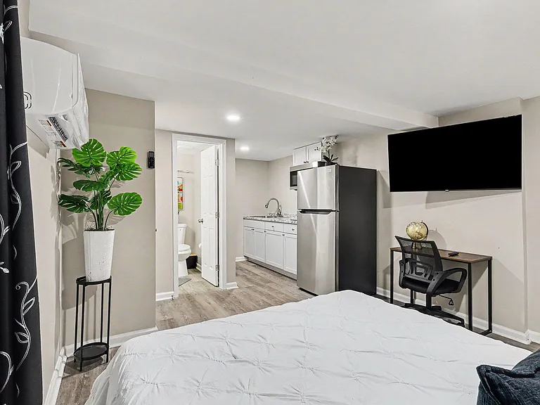 Furnished bedroom suite with a mini kitchenette, full-size refrigerator, and a dedicated desk area; bath access nearby.