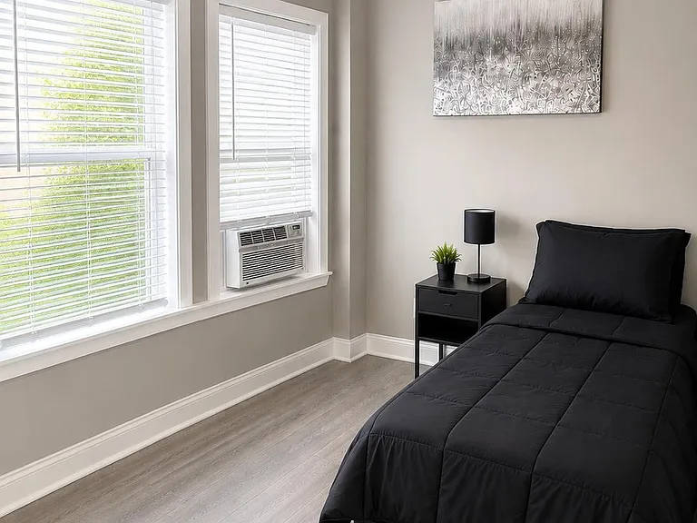 Private bedroom with two large windows, gray-tone flooring, and a nightstand setup for convenient bedside storage.