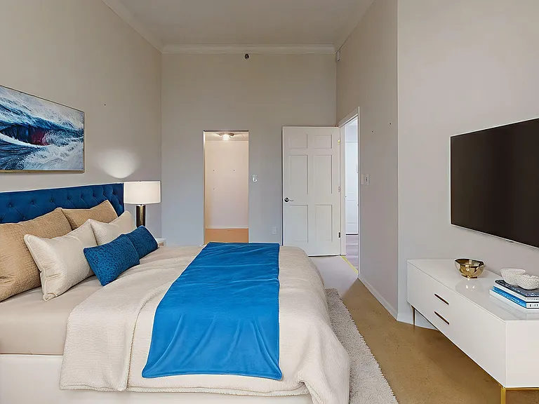 Luxurious bedroom with a plush blue headboard, vivid ocean artwork, and sleek modern decor for a serene ambiance.