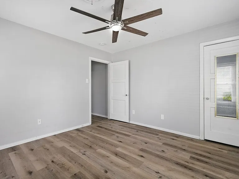 Large bedroom at the front of the house featuring neutral soft grey paint, LVP flooring, ceiling fan, closet and multiple windows