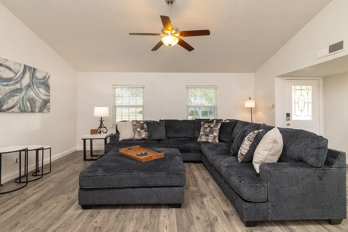Open and inviting living room featuring a cozy couch, oversized ottoman, ceiling fan for added comfort, flat-screen Roku TV, and a beautiful indoor fireplace that adds both warmth and character. - 864 Warwick Dr