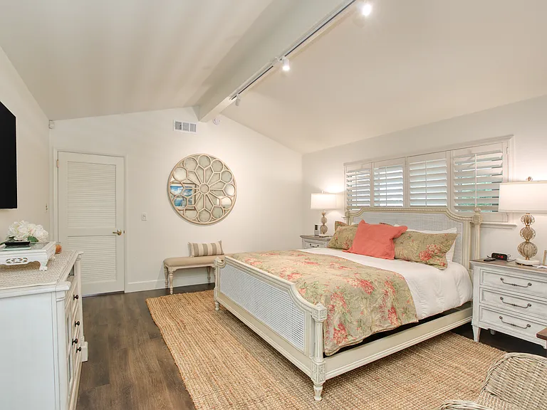 The spacious room showcases a plush king-sized bed framed by expansive windows that flood the space with natural light,