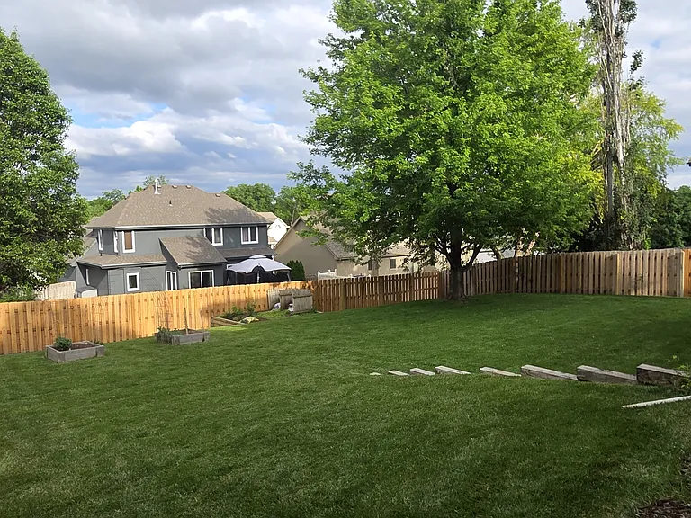 Backyard featuring large lawn, mature maple tree, deck with sliding door to kitchen, walkout basement, and raised garden beds.