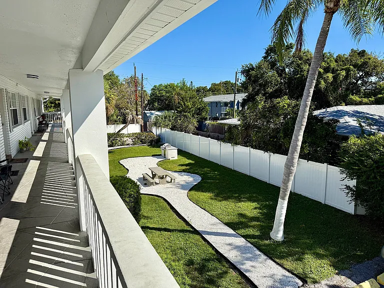 Charming apartment view featuring a sunny communal garden with a stylish pathway, picnic table, and lush greenery, perfect for outdoor relaxation.