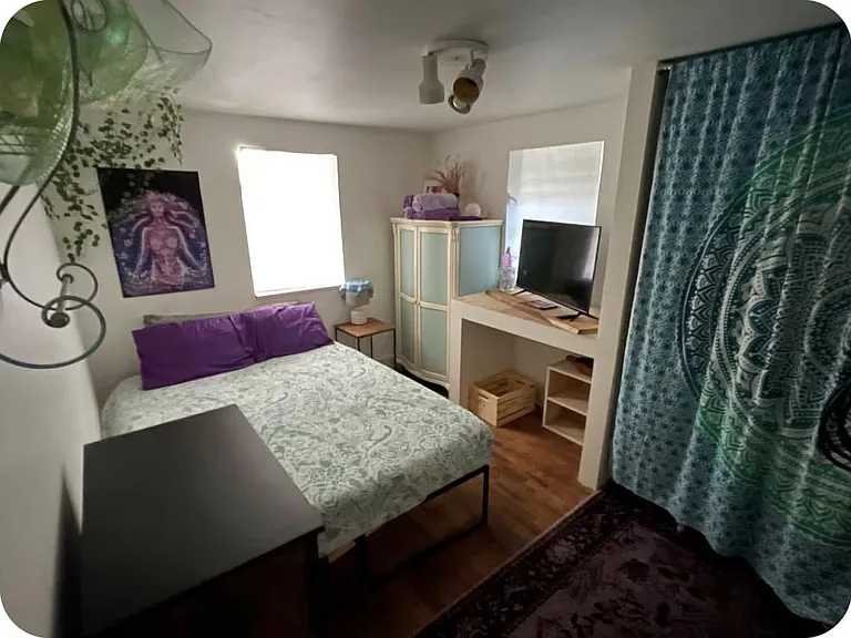 Private bedroom with a full bed, two windows, and wood-look flooring, plus a TV nook and storage cabinet for easy living.
