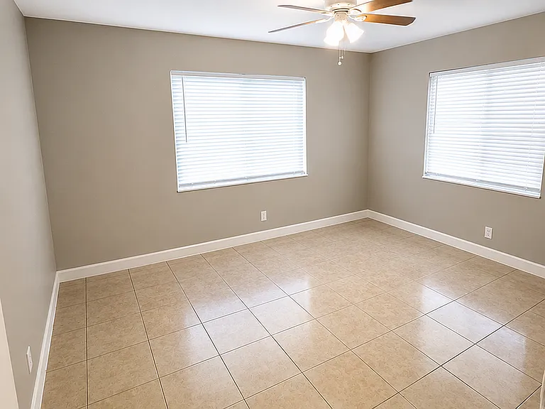 Bright and spacious room with elegant tile flooring, neutral walls, and large windows complemented by a modern ceiling fan.