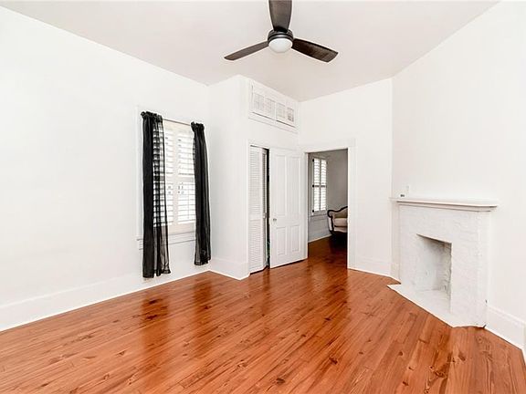 Room featuring wood-finish flooring, a white brick fireplace, and a ceiling fan