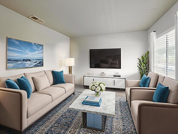 Chic modern living room with plush beige sofas, vibrant blue cushions, and a sleek marble coffee table. Elegant decor featuring stylish plants, artistic wall painting, and ample natural light.