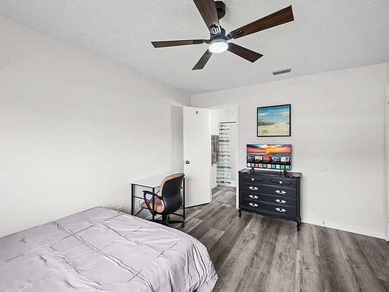 Spacious bedroom with ceiling fan, wood-look flooring, and a work desk, plus dresser and TV for easy daily living.