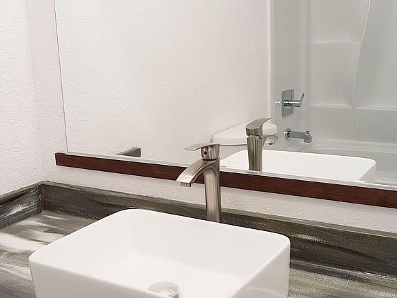 bathroom with a modern above-countertop sink and faucet, new bathtub, and toilet.
