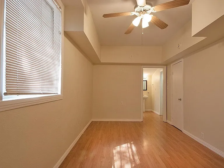 A cozy bedroom with a window featuring hardwood floors and a ceiling fan, perfect for keeping cool and comfortable.