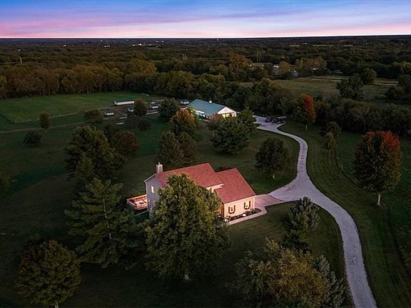 An expansive rural estate boasts mature trees, open pastures, and a private winding driveway.