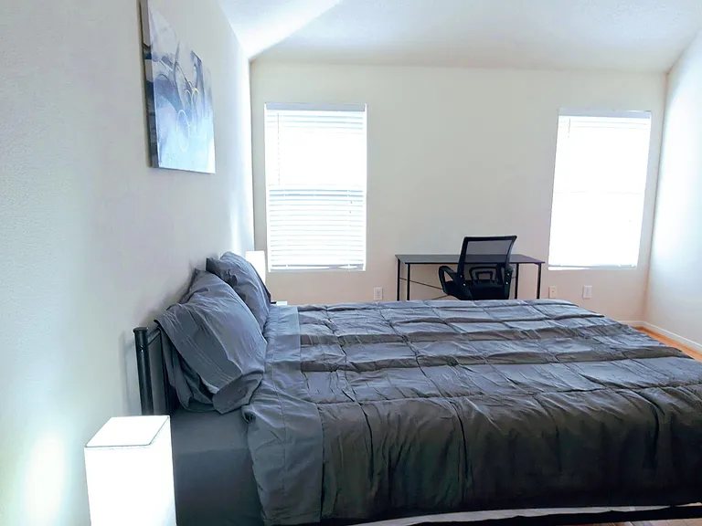 Spacious bedroom with vaulted ceiling, ceiling fan, two windows, and a dedicated desk area plus bedside storage.