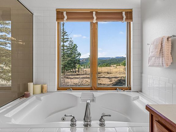 Spa-style soaking tub with tile surround and dual windows, offering relaxing views and convenient towel storage.