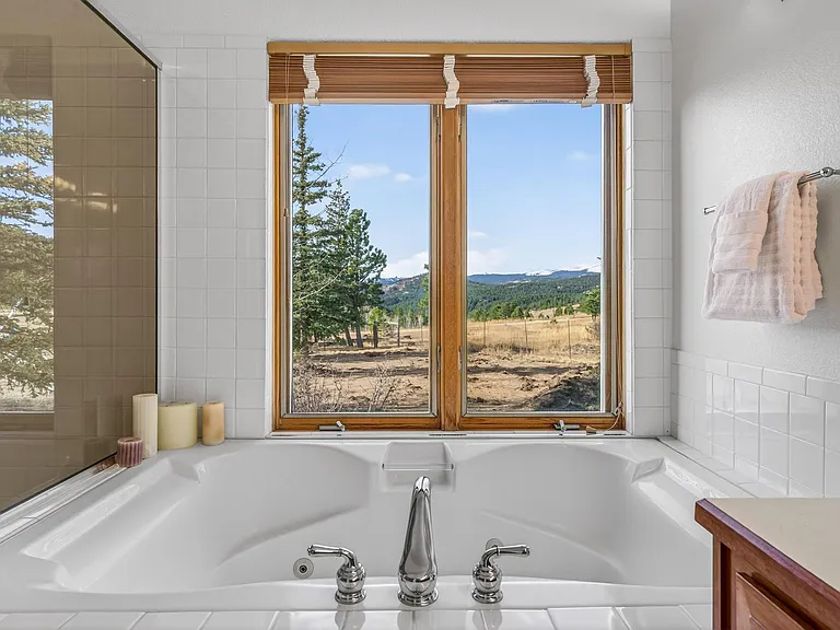 Spa-style soaking tub with tile surround and dual windows, offering relaxing views and convenient towel storage.