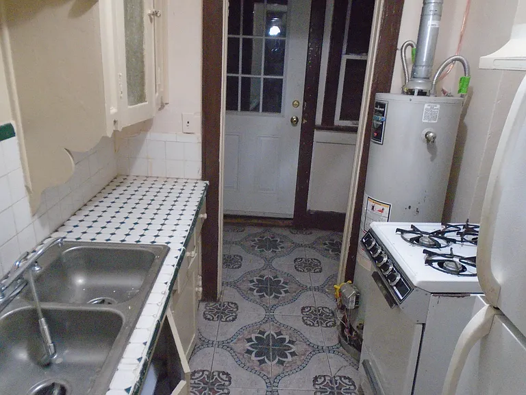 South looking view into the kitchen, including the stainless steel kitchen sink and full size 30 in gas range and ceramic tile floor.