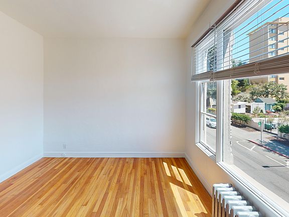 Bright room with hardwood floors and a large window overlooking a street and greenery outside